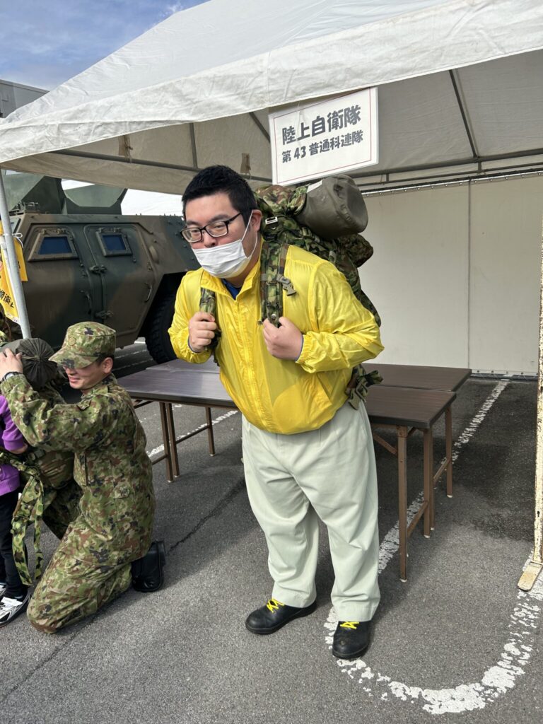 中尾社員による自衛隊装備品(３０kg）の背負い体験　非常に重そうです！